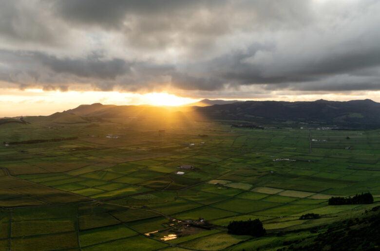 Sonnenuntergang über der grünen Hügellandschaft von Terceira, Azoren, mit Blick auf das fruchtbare Inselinnere und dramatische Wolken am Horizont