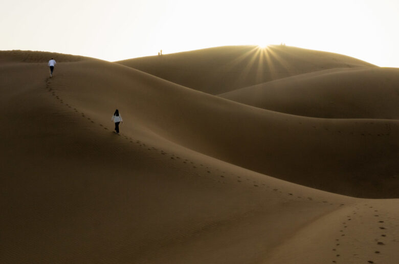 Menschen laufen bei Sonnenaufgang über Sanddünen in der Sahara, Marokko